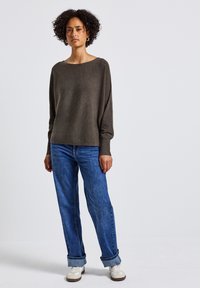 Maglione marrone a maglia con scollo ampio e maniche lunghe, abbinato a jeans in denim blu con vestibilità comoda. Sneakers bianche con dettagli marroni.