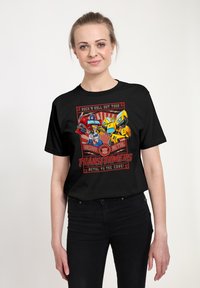 Černé tričko s barevnou grafikou "Transformers" z postavami a textem. Krátké rukávy a standardní střih. Hladká bavlněná tkanina.