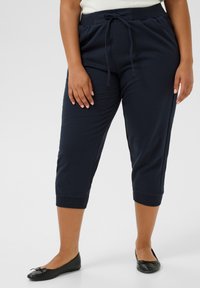 Pantaloni jogger cropped blu navy con vita regolabile, polsini a coste e una texture morbida, abbinati a ballerine nere.