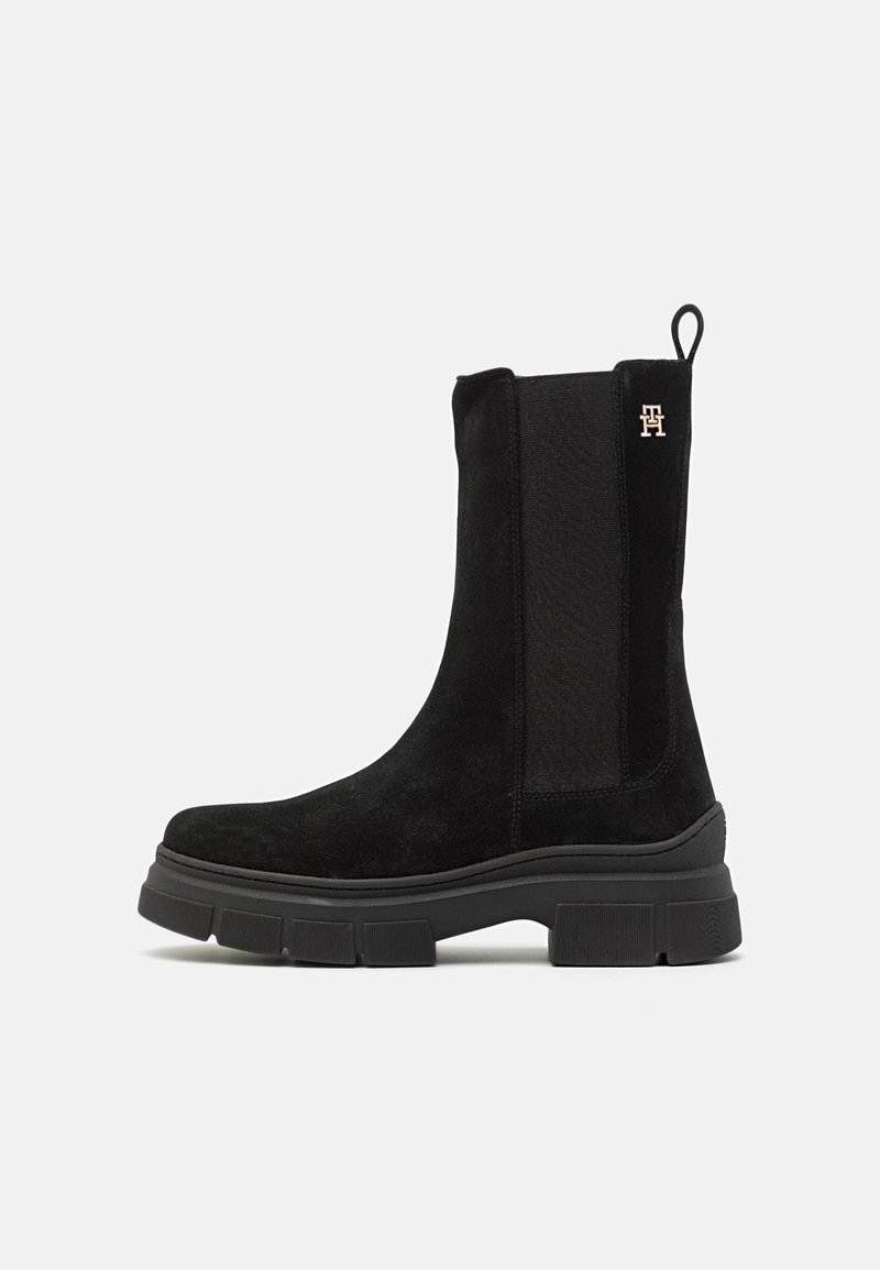 Botte noire en daim mi-mollet avec semelle épaisse, panneau latéral élastique, languette à l'arrière et petit logo doré près du sommet.
