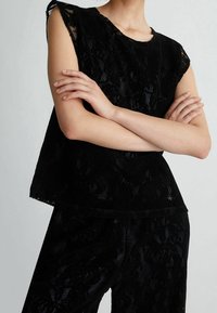 Top in pizzo nero con maniche corte e strutturate. Tessuto morbido con motivo floreale, design a strati e dettagli dell'orlo discreti.
