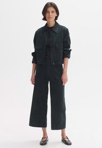 Dark green corduroy jacket with two front pockets, paired with matching wide-leg trousers and black flats. Smooth texture, relaxed fit.