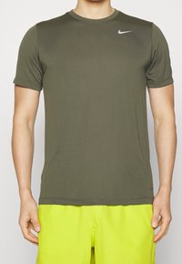 T-shirt sportivo Nike di colore verde oliva, maniche corte, texture liscia, scollatura a girocollo, con un piccolo logo bianco sulla spalla sinistra.