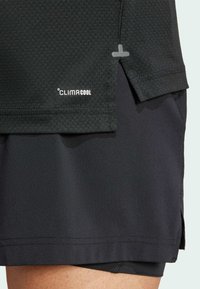 Camisa deportiva negra con un patrón texturizado, etiqueta CLIMACOOL y un diseño de dobladillo dividido, combinada con pantalones cortos negros.