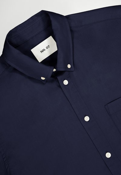 Navyblauwe overhemd met knopen, voorzien van een klassieke kraag, witte knopen, een zijzak op de linkerborst en een gladde, geweven textuur. Merklabel zichtbaar.