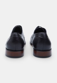 Scarpe in pelle nera con finitura liscia, punta rotonda e pannelli laterali testurizzati; tacco in legno marrone; dettagli di cucitura minimi sul retro.