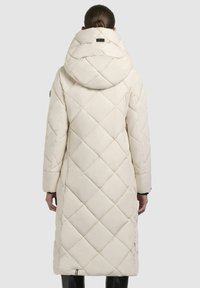 Cappotto lungo imbottito in crema con cappuccio. Presenta cuciture a rombi, tasche laterali e un'etichetta logo nera sul collo.