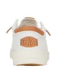 Sneaker bianca in tela con un accent in pelle color tan, caratterizzata da un logo circolare "HEY DUDE" ricamato nel tallone e lacci elasticizzati.