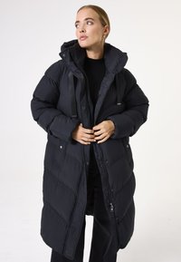 Manteau long en doudoune noir avec capuche, design matelassé, fermeture éclair à l'avant et pressions, et sangles ajustables. Texture lisse, coupe décontractée.