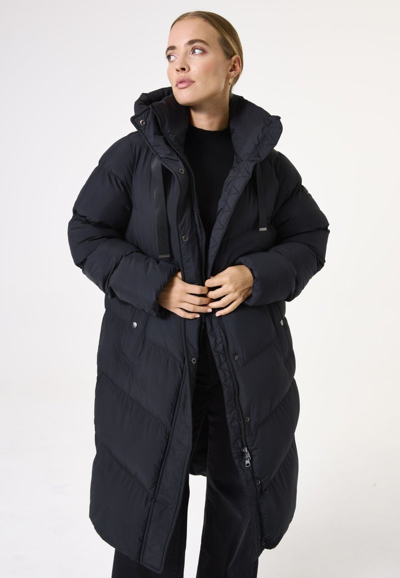 Manteau long en doudoune noir avec capuche, design matelassé, fermeture éclair à l'avant et pressions, et sangles ajustables. Texture lisse, coupe décontractée.