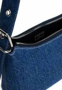Blauwe denim schoudertas met een zilveren rits, voorzien van een gladde textuur en een stevige schouderband. Binnenin staat het merklogo in het zwart.