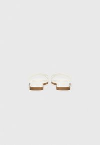 White flat sandals with a smooth texture, featuring thin straps and a light brown sole. Minimalist design with no visible logos or patterns.