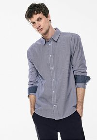 Košile na knoflíky s tenkými vertikálními pruhy v odstínech modré a bílé. Obsahuje rozepnutý límec, dlouhé manžetové rukávy a volný střih.
