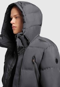 Hallhallikatehall, millel on suur kapuuts. Sellel on tõmblukuga esiosa, küljetaskud ja kerge sära. Õlal on brändingu detail.