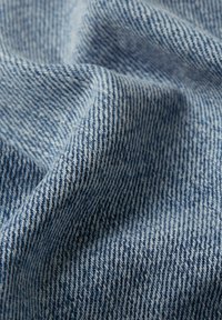 Tela de mezclilla azul claro con una fina textura de sarga, que muestra una mezcla de hilos azules y blancos, enfatizando una apariencia suave y tejida.