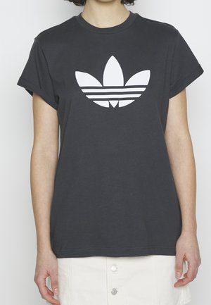 Tummanharmaa puuvillapaita, jossa on käärityt lyhyet hihnat ja suuri valkoinen Adidas-trefoillogo, jonka alla on kolme raitaa.