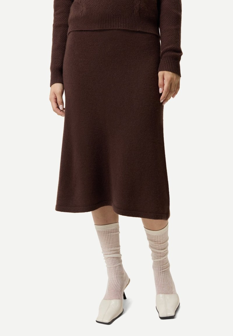 Femme portant une jupe midi en maille marron, un pull marron assorti, des chaussettes côtelées rose pâle et des talons blancs à bout carré.
