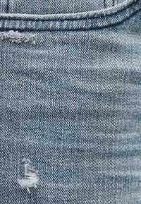 Tela de mezclilla azul claro con un aspecto desgastado, que presenta una pequeña área desgastada y una textura suave. Detalles visibles de estilo de cinco bolsillos.