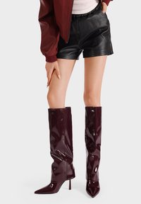 Stivali alti fino alla coscia in pelle verniciata bordeaux, con punta affusolata e tacco a stiletto, caratterizzati da una texture liscia e lucida e un design morbido.