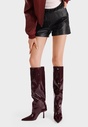 Stivali alti fino alla coscia in pelle verniciata bordeaux, con punta affusolata e tacco a stiletto, caratterizzati da una texture liscia e lucida e un design morbido.