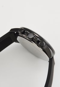Sorte armbåndsur med rund kasse, tre knapper og strukturert stropp. Har en glatt overflate og minimalistisk design på urskiven.