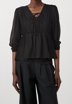Zwarte, lichte blouse met een V-hals, een strikdetail bij de halslijn en driekwart mouwen. Peplum ontwerp met een doorzichtige textuur.