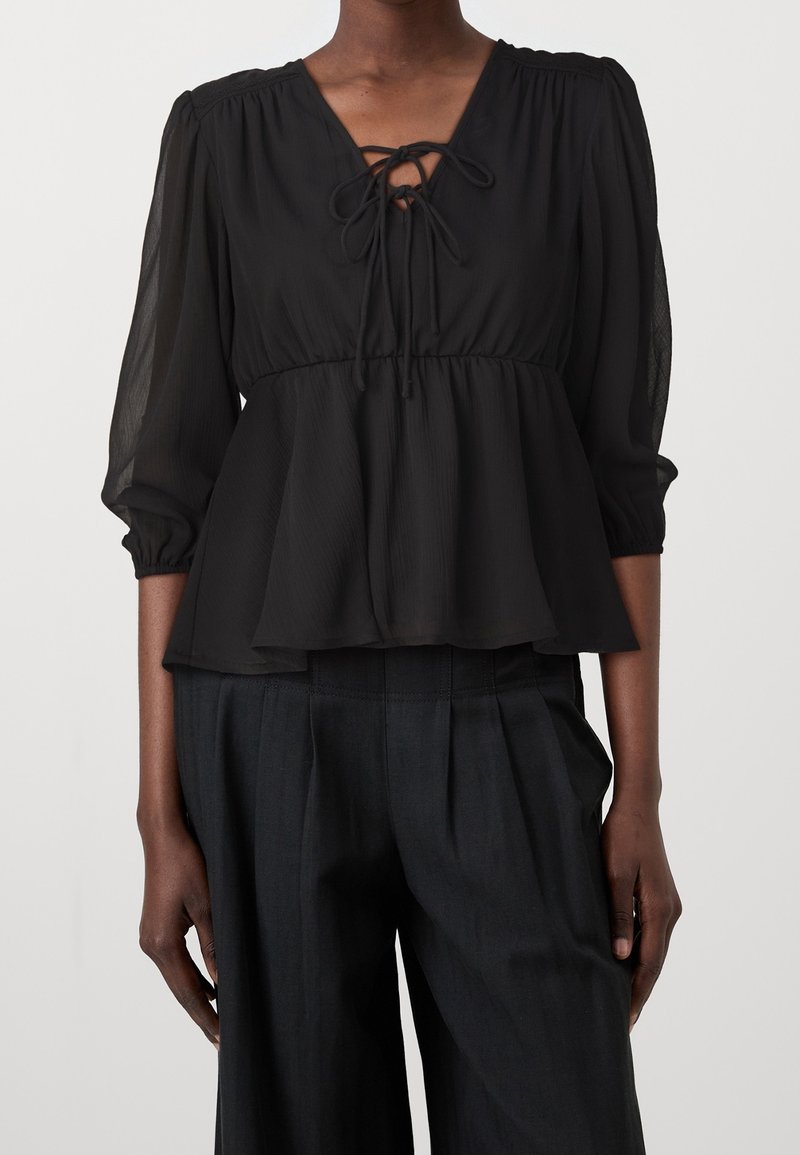Svart, lätt blus med V-hals, en knytdetalj vid halsen och trekvartslånga ärmar. Peplumdesign med genomskinlig struktur.