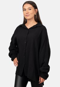 Camicia nera oversize con bottoni realizzata in tessuto testurizzato, con colletto e maniche lunghe, caratterizzata da una vestibilità rilassata e spalle scese.