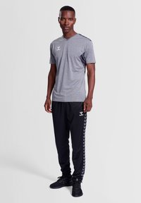 Grijze sport T-shirt met korte mouwen en een V-hals, gecombineerd met zwarte trainingsbroeken voorzien van een zijwaarts visgraatpatroon en logo.