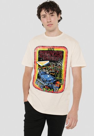 Beige Grafik-T-Shirt mit einem retro "Stranger Things"-Design, das ein Auto, Arcade-Elemente und lebendige Farben in verschiedenen Mustern zeigt.
