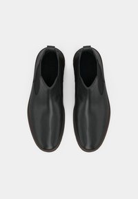 Botas chelsea de couro preto com painéis laterais elásticos, bico redondo, sola castanha, textura suave e alças para fácil calçar.