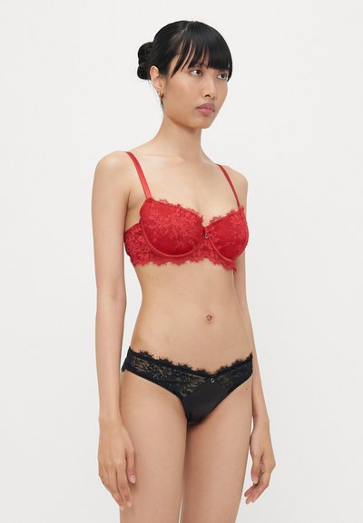Red lace bra with underwire and adjustable straps, paired with black lace-trimmed thong. Delicate floral patterns throughout.