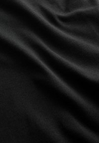 Nahaufnahme eines glatten, schwarzen, gerippten Stoffs mit sanften Falten, die weiche Schatten und Textur erzeugen.