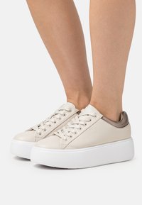 Sneakers piattaforma in pelle beige con suole bianche. Presentano punta rotonda, design con lacci e dettagli metallici sul tallone. Texture liscia.