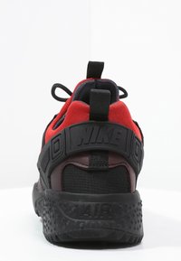 Punainen ja musta lenkkikenkä, jossa on teksturoitu kumipohja, korostettu korko, pehmustettu verkkoyläosa ja näkyvä "AIR"-brändäys takana.