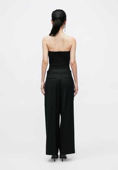 Melna, bezsiksnu augšdaļa, kas kombinēta ar melnām plašām biksēm. Apģērbs ir ar tīru dizainu, pieguļoša vidukļa līniju un rāvējslēdzēju aizmugurē.