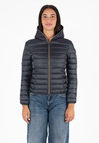 Donkergrijze pufferjack met een ritssluiting aan de voorkant en een capuchon. Kenmerkt zich door gestikte horizontale panelen en een aangesloten design, gecombineerd met blauwe denim jeans.