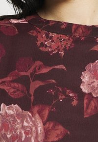 Mörkröd tyg med ett blommönster som har stora rosiga blommor i nyanser av rosa och röd, tillsammans med gröna blad och ömtåliga detaljer.