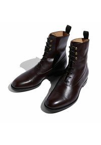 Stivaletti in pelle marrone con punta rotonda, finitura liscia e chiusura con lacci, dotati di occhielli in metallo e una linguetta sul retro.