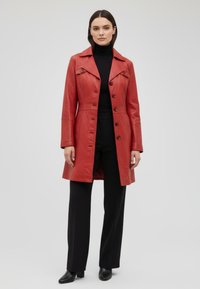 Red leather coat with a fitted design, notched collar, button-up front, and long sleeves. Paired with black turtleneck and trousers.