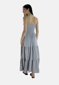 Abito maxi grigio con corpetto arricciato, spalline sottili e gonna a strati. Tessuto morbido e design fluido, che giunge fino alle caviglie.