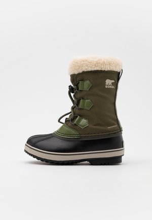 Botte d'hiver imperméable verte et noire avec bord en peau de mouton beige, laçage devant et logo Sorel sur le côté.