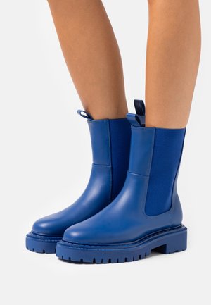Botas de tobillo azul hechas de cuero suave con paneles laterales elásticos, punta redonda y suela de goma gruesa y texturizada para mayor tracción.