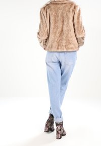 Béžová bunda z umělé kožešiny, modré džíny volného střihu a květinové kotníkové boty s robustním podpatkem. Měkká textura kontrastuje s denimem.