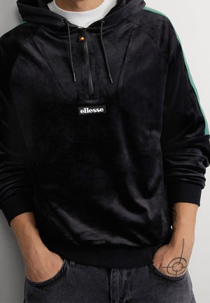 Schwarze Velours-Hoodie mit einem Viertelreißverschluss, grünen Schulterstreifen und einem Logo-Patch auf der Vorderseite. Rippbündchen und -saum, weicher Stoff.