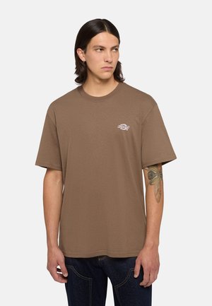 Camiseta de algodón marrón con corte holgado y mangas cortas, con un pequeño logo blanco en el lado izquierdo del pecho. Textura suave y diseño sencillo.