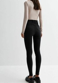 Leggings negros de cintura alta con un ajuste ceñido, que presentan una textura suave y bolsillos traseros. Combinados con zapatos negros.