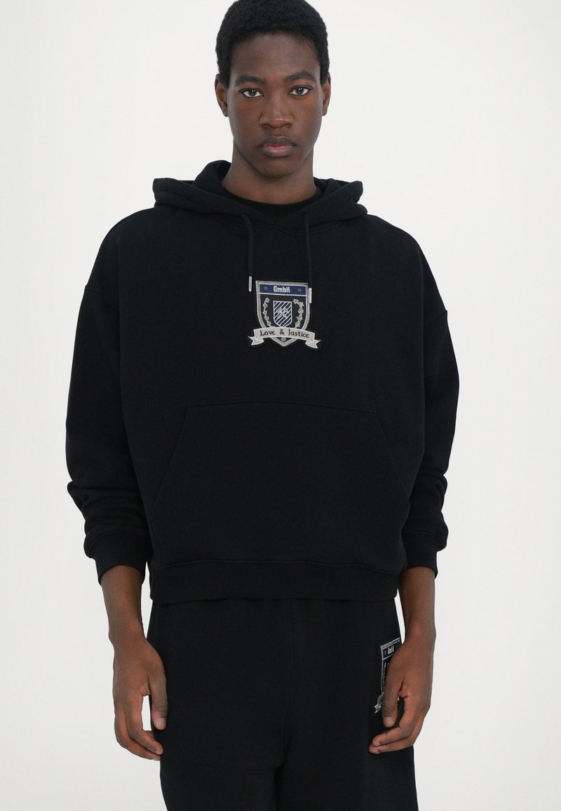 Black hoodie made of soft fabric, featuring a front pocket, drawstring hood, and embroidered badge with "Love & Justice" text.