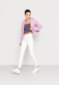 Hoodie cropped rosa claro, top cropped às riscas azul marinho, jeans skinny brancos e ténis brancos; os acessórios incluem uma pequena mala com alça em corrente.