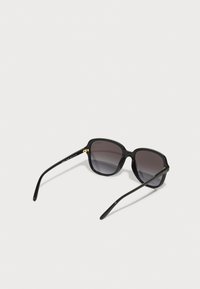 Ochelari de soare negri, hexagonali, cu lentile gri degradate. Cadru din plastic lucios și brațe negre elegante. Accente aurii lângă balama.